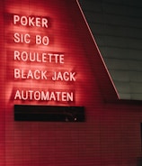 Red neon letters are mounted on a dark tiled wall, displaying the words Poker, Sic Bo, Roulette, Black Jack, and Automaten.