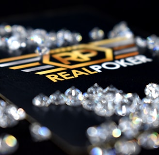 A collection of sparkling, clear gemstones surrounds a dark surface featuring the prominent logo and text 'Real Poker.' The logo design includes gold and white elements set against a black background.