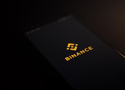A smartphone screen displaying the Binance logo with yellow text and an icon in the center against a dark background.