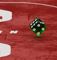 Two green dice with rounded edges are positioned on a red surface that seems to be part of a game board. The surface has white text and numbers on it, including the word 'LUCKYTOPSPIN' in capital letters.
